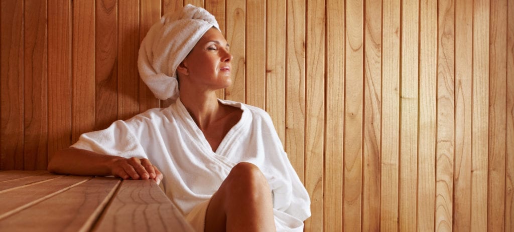 Woman in robe and towel on head in sauna relaxing with her eyes closed