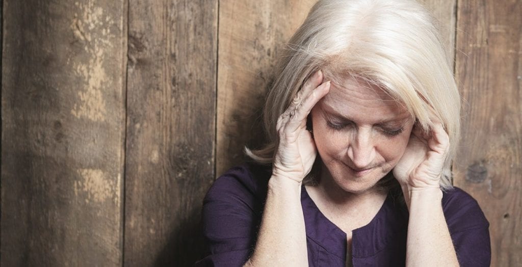 A depress senior woman with wood background; highlighting depression as a symptom of menopause