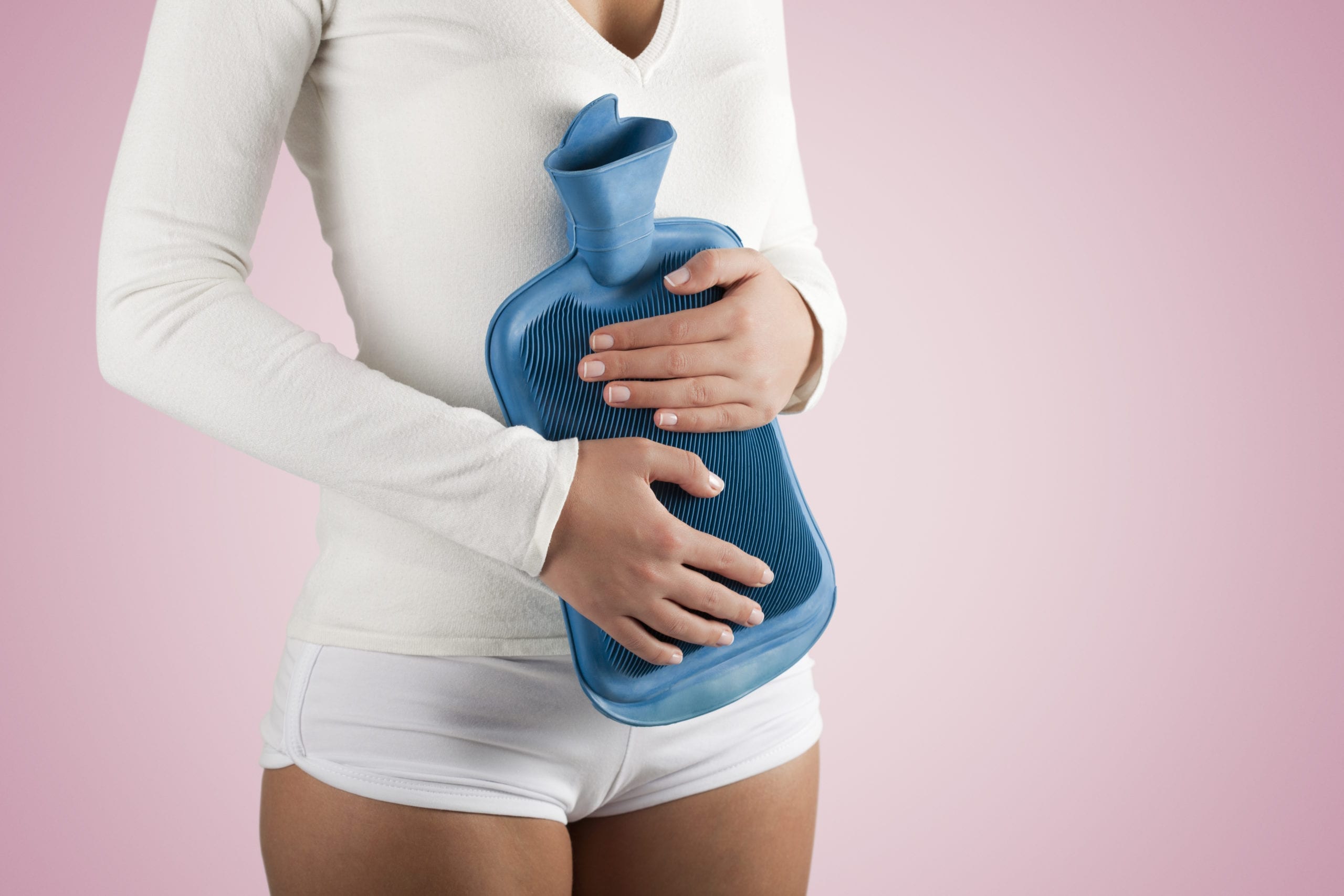 Woman having stomachache, holding with hot water bottle on pink background; highlighting the symptoms of SIBO
