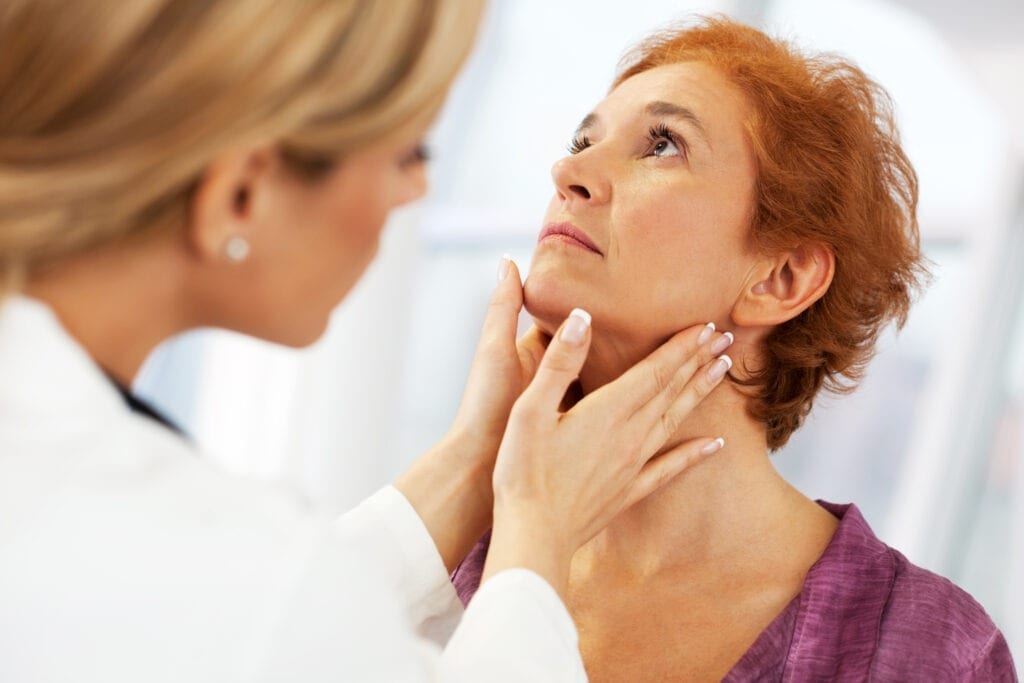 Close-up of a female doctor doing a medical examination. The focus is on the mature adult woman being examined in a thyroid exam