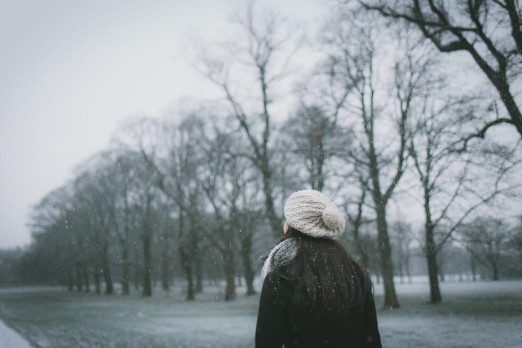 woman walking in light snow with trees in the background on a grey day; highlighting Seasonal Affective Disorder