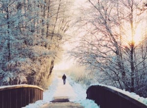 Man walking outside in the snow on a path over a bridge taking time for selfcare to survive the holidays
