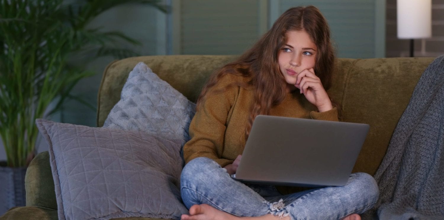 Thoughtful teenage girl with laptop on sofa suffering from headaches due to stress. This article outlines that mindfullness may be help.