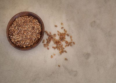 Flax seeds in a brown bowl with some sprinkled on table top; highlighting that flax can be used as an egg alternative in these quinoa cookies