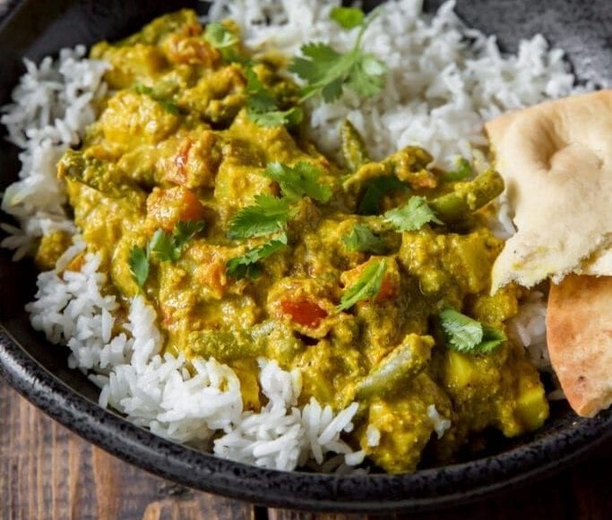 Creamy Indian Korma Over Rice in a black enamel bowl.