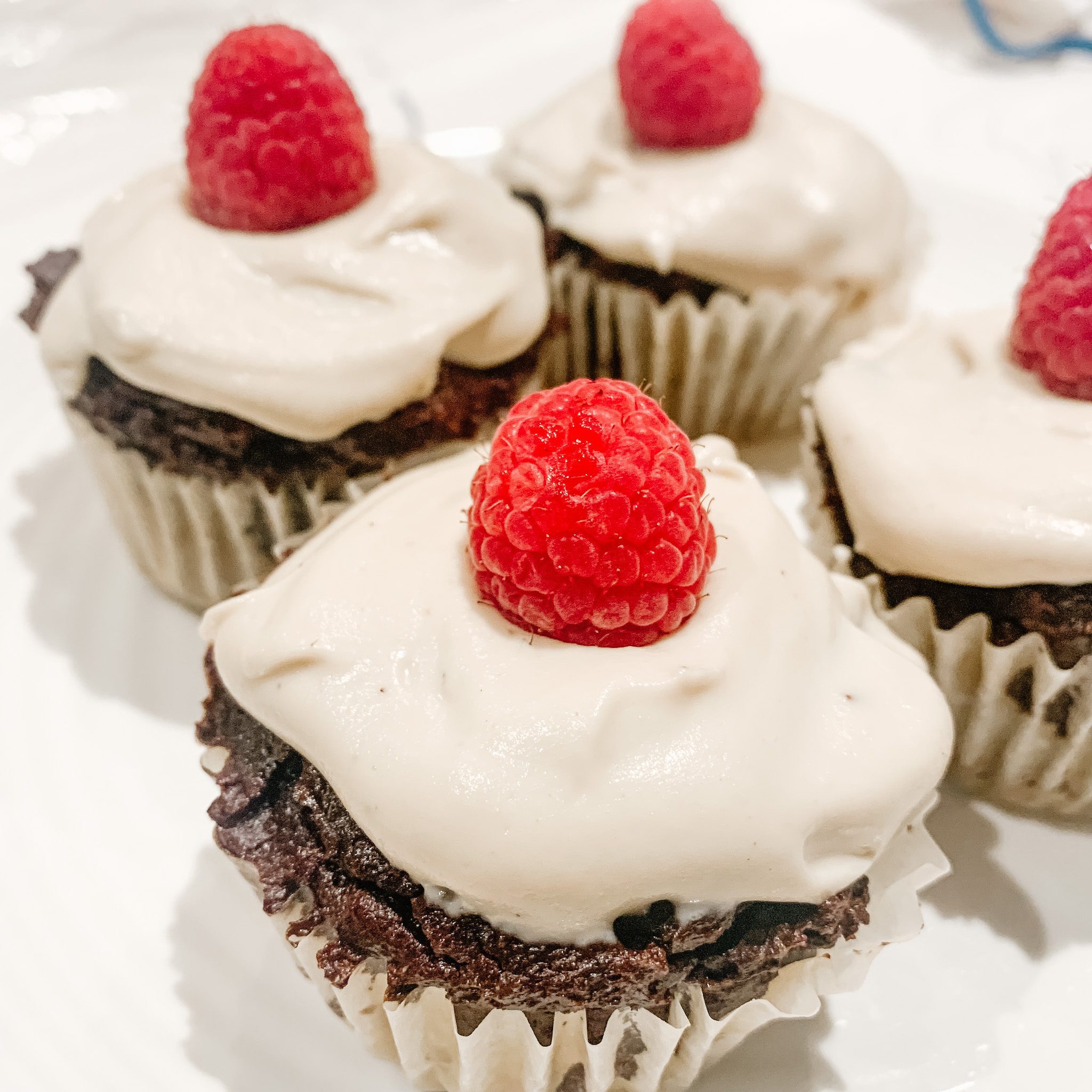 dairy free cashew vanilla icing on four chocolate cupcakes with a raspberry on top
