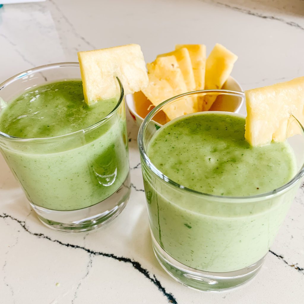 green gut healing smoothie in two glasses on a stone counter with pineapple chunks as garnish