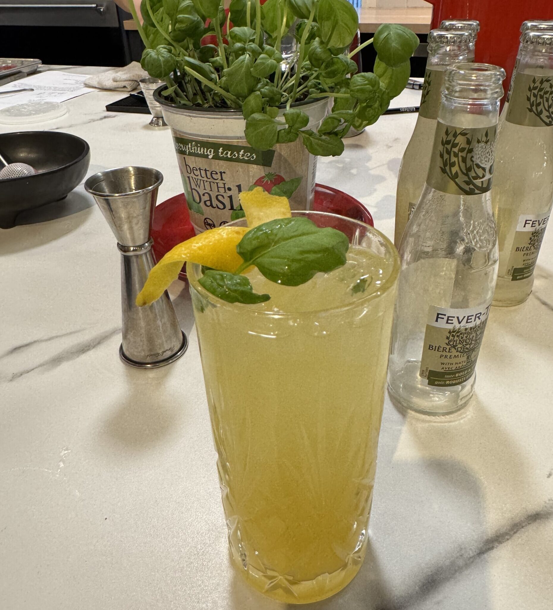 Tall Collins glass with pineapple mule mocktail in it, garnished with lemon peel and fresh thai basil.